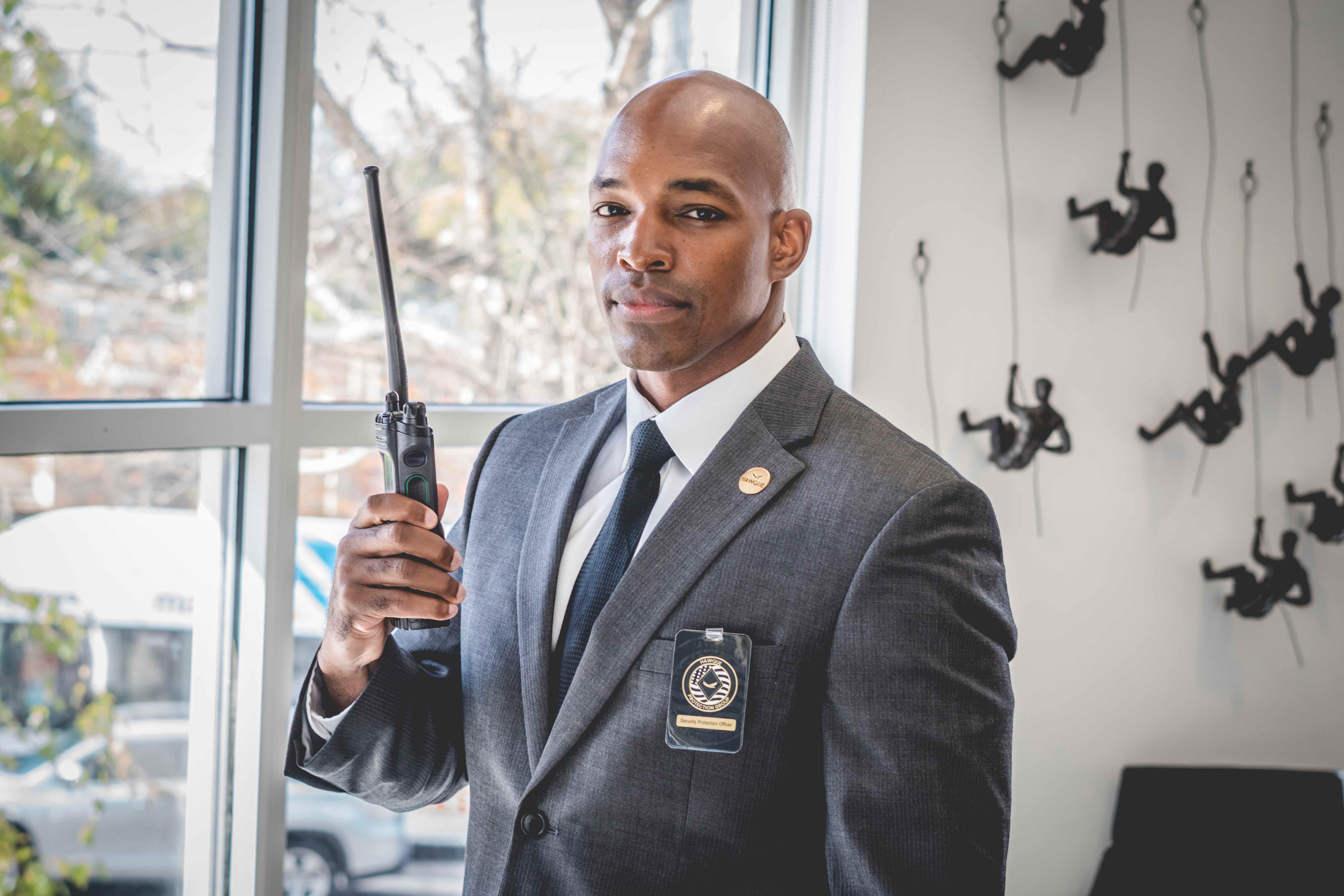 A Hawque protection professional in business attire coordinating by radio from a modern property lobby.